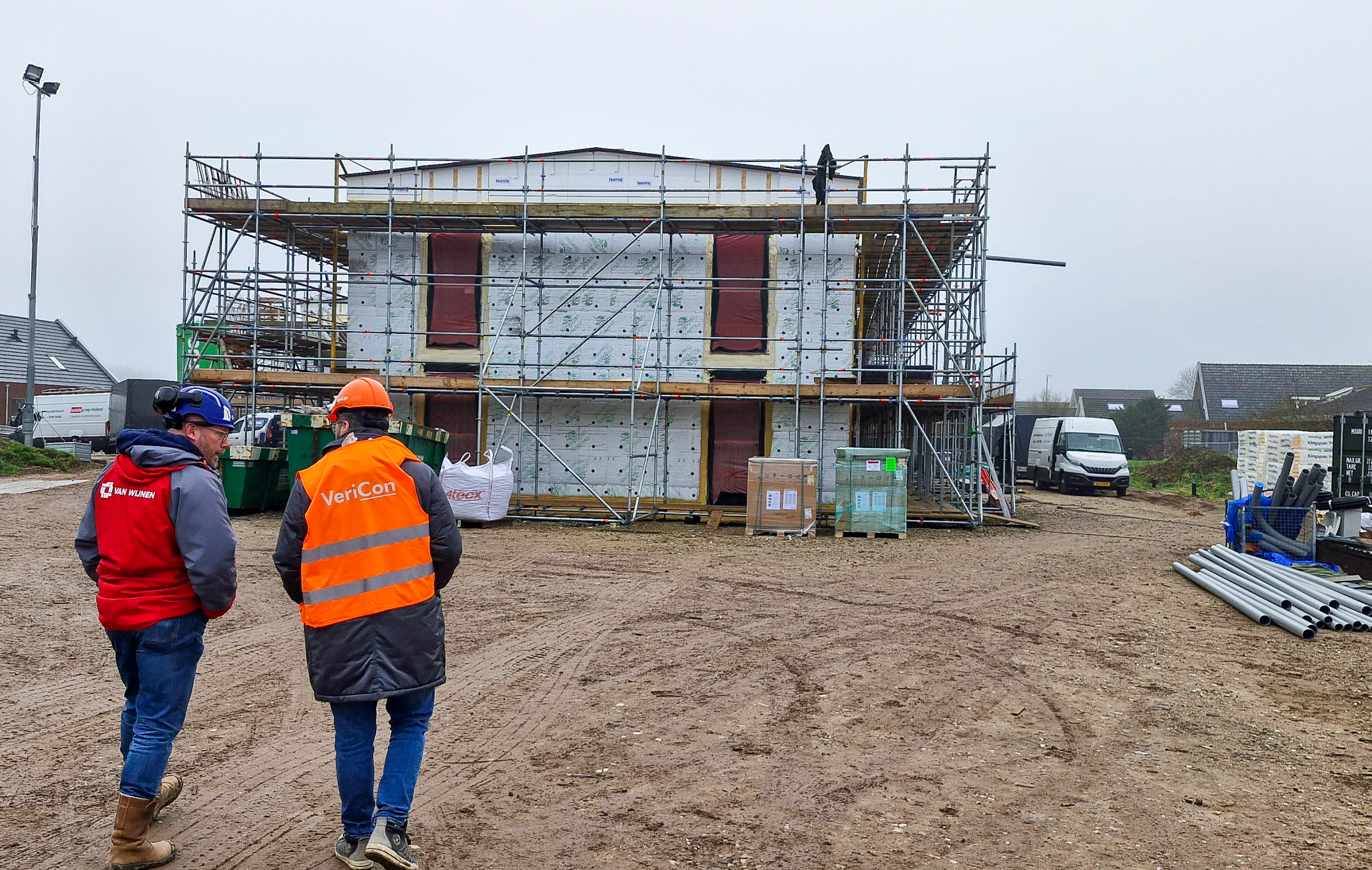 Twee bouwvakkers lopen naar gebouw in aanbouw.