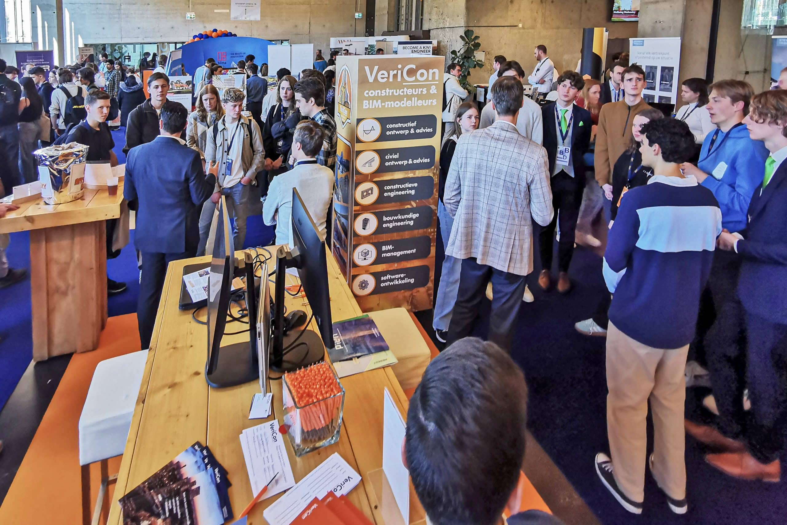 Mensen verzamelen zich rond een informatiestand op een beurs.