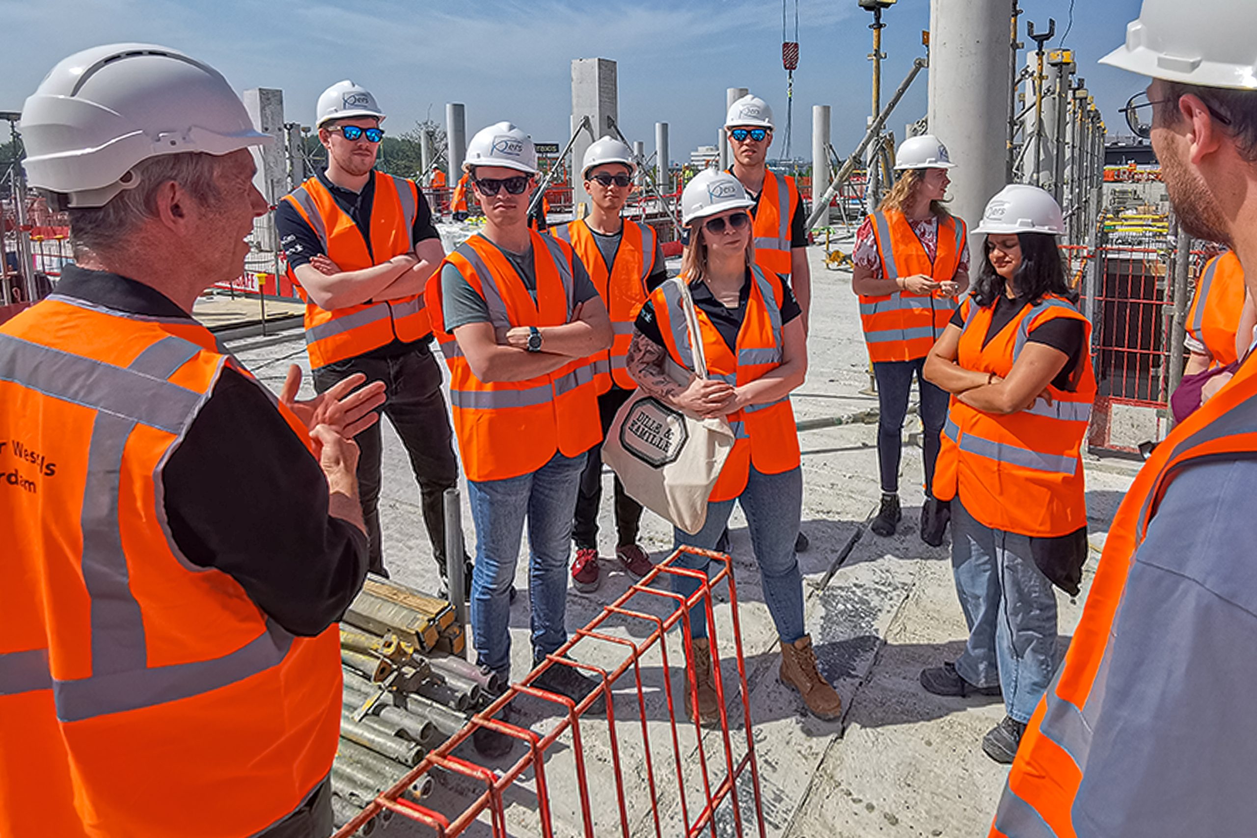 Groep mensen op bouwplaats met oranje veiligheidskleding.